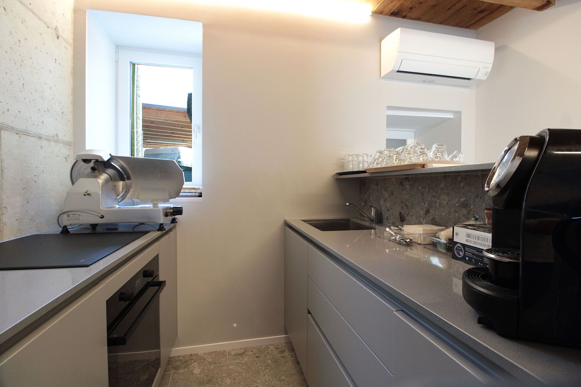 A compact kitchen with a built-in coffee machine, a sink, and a window with blinds.