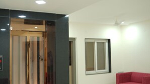 Een moderne hotellobby met een glazen lift, een rode bank en een groot raam.