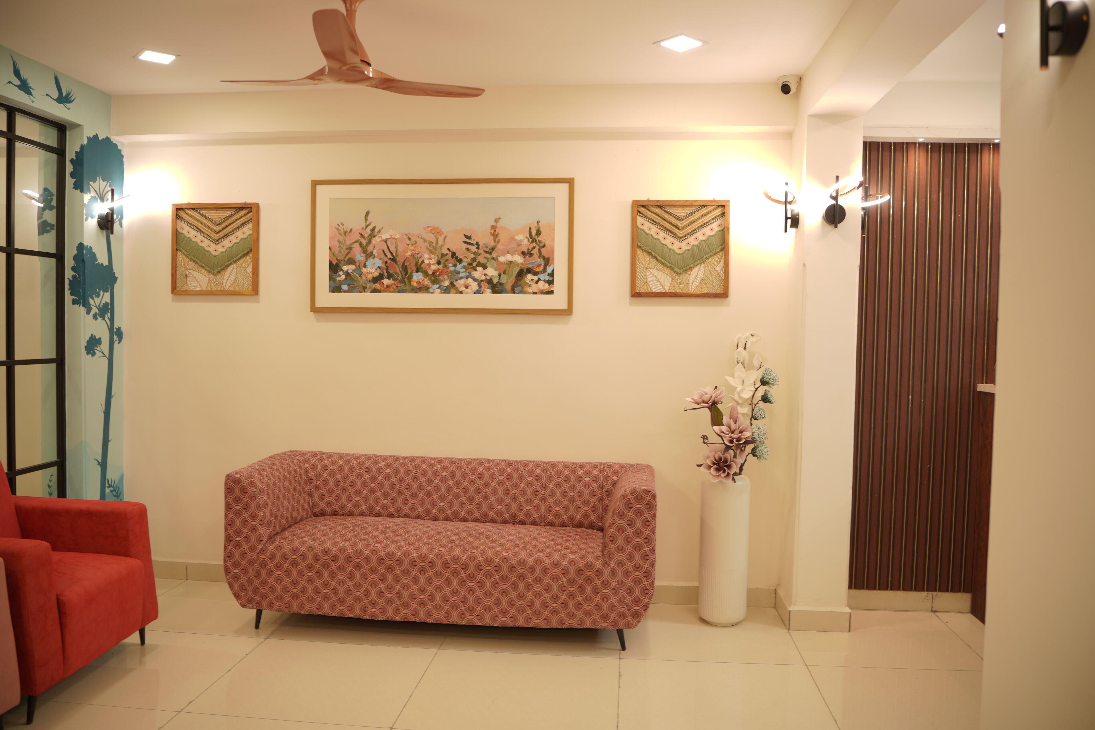 A living room with a patterned sofa, a red armchair, a ceiling fan, and wall-mounted artwork.