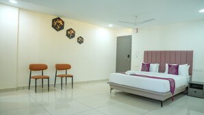 Een hotelkamer met een bed, twee stoelen, een plafondventilator en wanddecoratie.