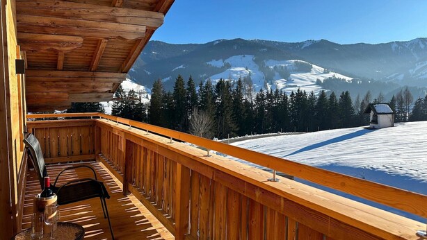 Un balcon en bois offrant une vue sur des montagnes enneigées et une petite cabane.