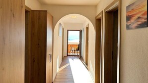 Un couloir au plancher et aux portes en bois, qui mène à une pièce offrant une vue sur le ciel.