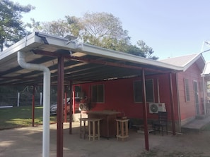 A red building with a covered patio area, a fan, and a table with stools.