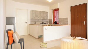 A compact kitchen with a central island, a refrigerator, and a wooden door. - Cozy Apartment with free private parking (Alghero)
