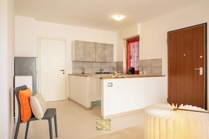 A compact kitchen with a central island, a refrigerator, and a wooden door. - Cozy Apartment with free private parking (Alghero)