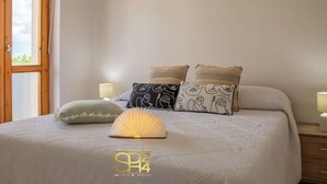 A bedroom with a bed, pillows, a bedside lamp, and a window. - Cozy Apartment with free private parking (Alghero)