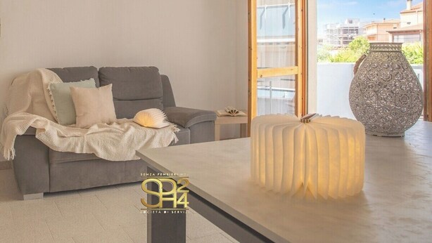 A modern living room with a grey sofa, a white ottoman, and a decorative vase. - Cozy Apartment with free private parking (Alghero)