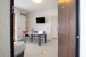 A modern interior with a dining area, a mounted TV, and a wooden door. - Cozy Apartment with free private parking (Alghero)