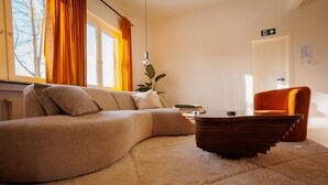 Ein modernes Wohnzimmer mit einer gebogenen Couch, einem einzigartigen Holztisch und einem leuchtend orangefarbenen Sessel.
