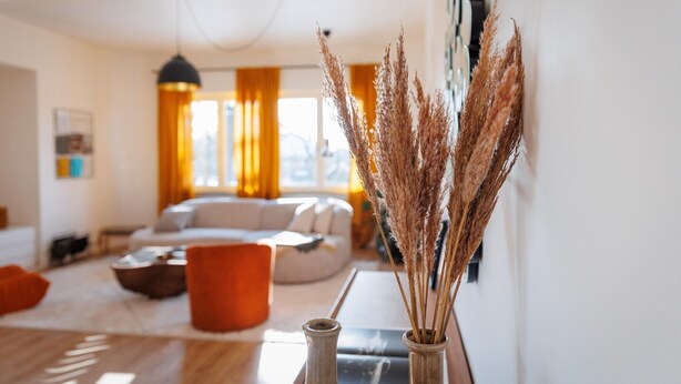 Ein Wohnzimmer mit einer Couch, einem Couchtisch und einer Vase mit Trockenblumen.