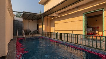 Piscina com deck revestido e pequena área de estar com cadeiras.