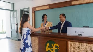 Un comptoir d’accueil avec un logo, un homme et une femme se serrant la main, et une porte en arrière-plan.