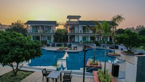 A hotel with a swimming pool, outdoor seating, and a view of the sunset. - Trideus The Wild Fraser Corbett (Kaladhungi)
