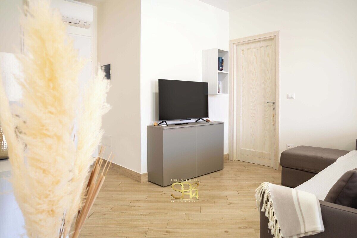 Un salon moderne avec un téléviseur à écran plat posé sur un meuble gris, un canapé marron et une porte visible au fond.
