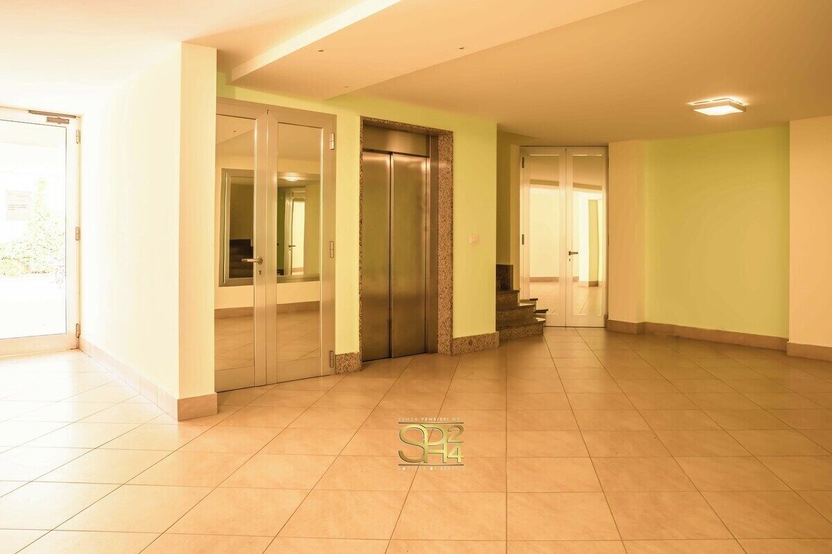 A spacious, well-lit hallway with a modern elevator and a door leading to a staircase.