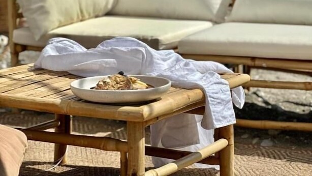 Un espace de détente aménagé sur la plage, avec des sièges confortables, une table sur laquelle est disposée une assiette de nourriture et des meubles en bambou.