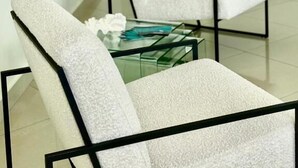 Un salon moderne avec une table basse en verre, un fauteuil blanc et une structure en métal noir.