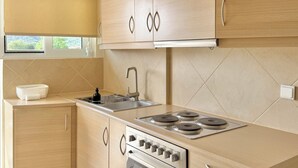 Une cuisine moderne avec des meubles en bois clair, une cuisinière en acier inoxydable et une fenêtre donnant sur un paysage verdoyant.