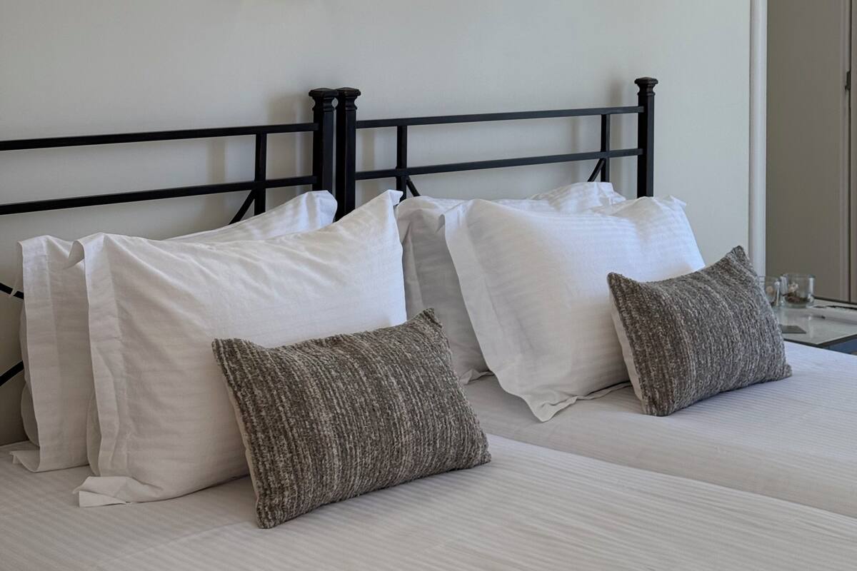 Habitación de hotel con cama, almohadas, una lámpara fijada a la pared y una puerta.