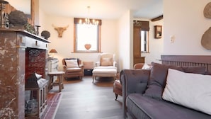 A cozy living room with a fireplace, a chandelier, a cow skull wall decoration, and a large window. - Spacious gite in Somme-leuze (Heure)