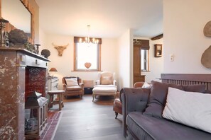 Ein gemütliches Wohnzimmer mit Kamin, einer Chandelüster und einer Wanddekoration aus einem Kuhschädel, sowie einem großen Fenster.