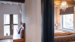 A room with a wooden bench, a bed with a leopard print bedspread, a chandelier, and a window with a view. - Spacious gite in Somme-leuze (Heure)
