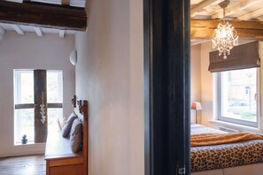 A room with a wooden bench, a bed with a leopard print bedspread, a chandelier, and a window with a view. - Spacious gite in Somme-leuze (Heure)