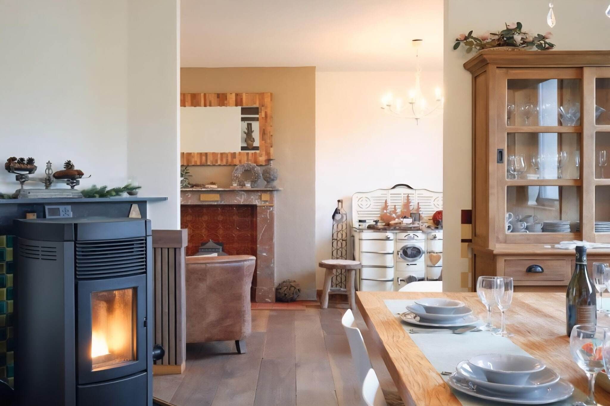 A cozy dining area with a wood-burning stove, a dining table set for two, and a cabinet with glass doors.