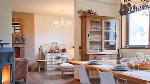 A cozy kitchen with a wood stove, dining table, chairs, and a cabinet with glassware. - Spacious gite in Somme-leuze (Heure)