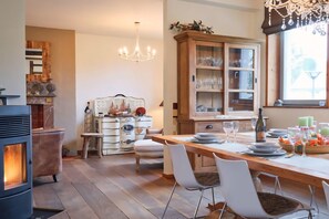 Eine gemütliche Küche mit Holzofen, Esstisch, Stühlen und einem Schrank mit Gläsern.