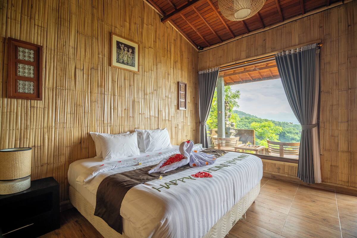 A wooden room with a bed, a nightstand, and a window with curtains.