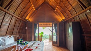 Een kamer met houten vloeren, een bed, een kledingkast en uitzicht op groen.