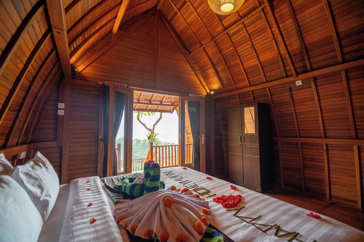 A cozy, wooden cabin room with a bed, a window, and a view of greenery outside.