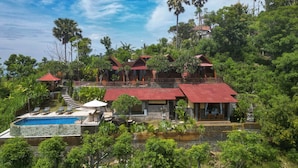 Een resort met meerdere villa's met rode daken, omgeven door weelderige groene begroeiing, een zwembad en een stenen trap naar de villa's.