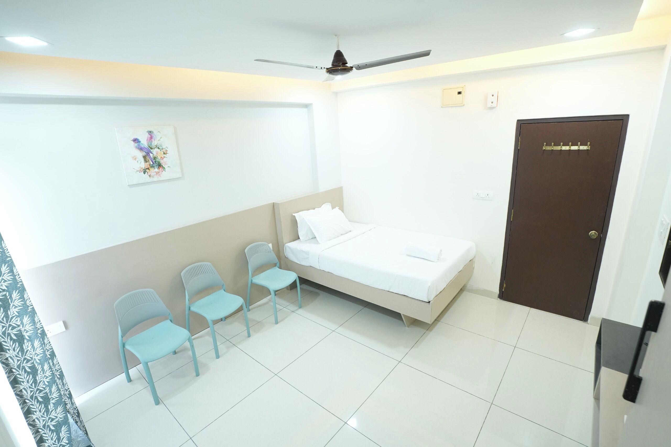 A bedroom with a bed, two chairs, a ceiling fan, and a door.