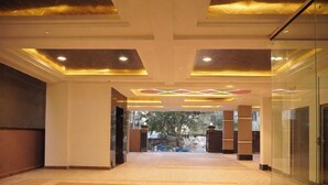 A spacious lobby with a tiled floor, a glass partition on the right, and a view of the outside through a glass door. - Hotel Flamount Arka Studios (Hyderabad)