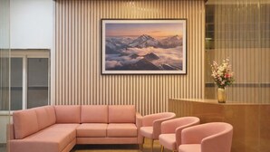 A modern reception area with a pink sectional sofa, matching chairs, and a framed mountain landscape painting on the wall. - Hotel Flamount Arka Studios (Hyderabad)