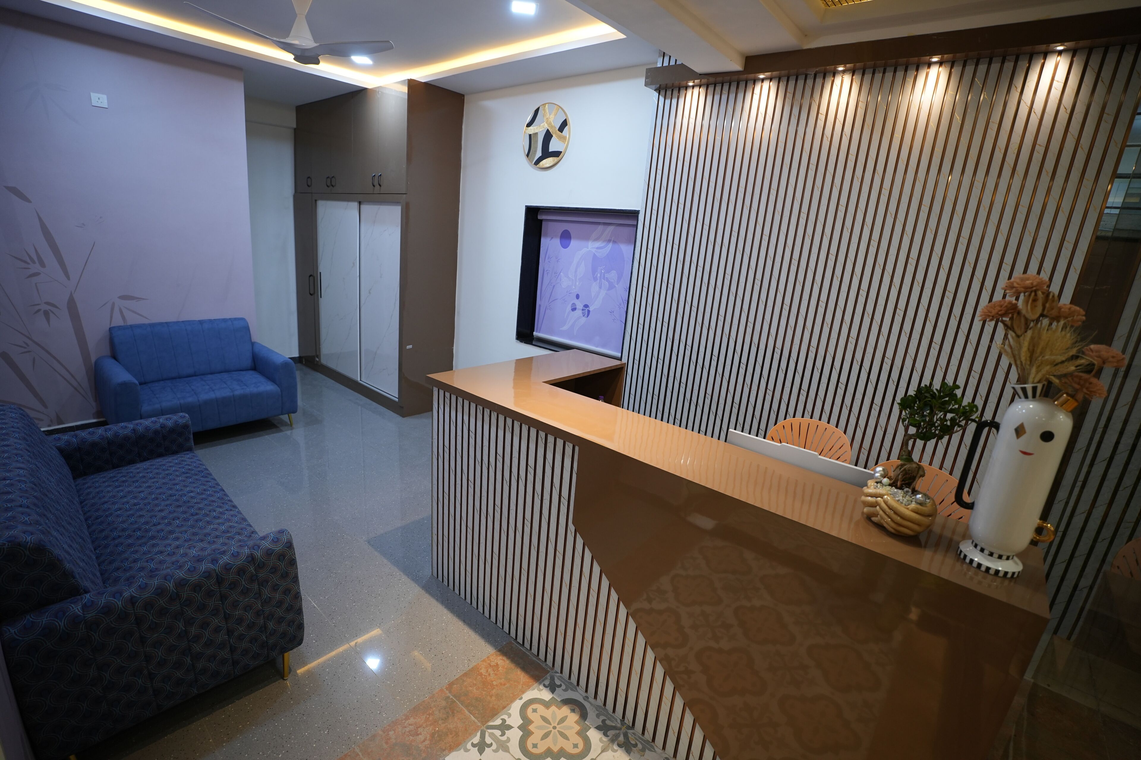 A reception area with a reception desk, a blue sofa, a television, and a decorative plant.