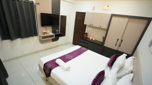 A neatly arranged hotel room with a bed, a TV, a wardrobe, and a small shelf with toiletries. - Hotel Flamount Arka Studios (Hyderabad)