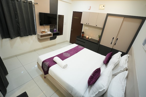 Una camera d'albergo ordinata con un letto, una televisione, un armadio e un piccolo ripiano con articoli da toilette.