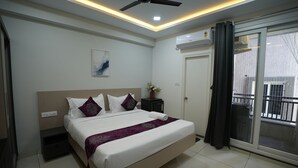 A modern bedroom with a bed, ceiling fan, air conditioning unit, and a view of the outside balcony. - Hotel Flamount Arka Studios (Hyderabad)