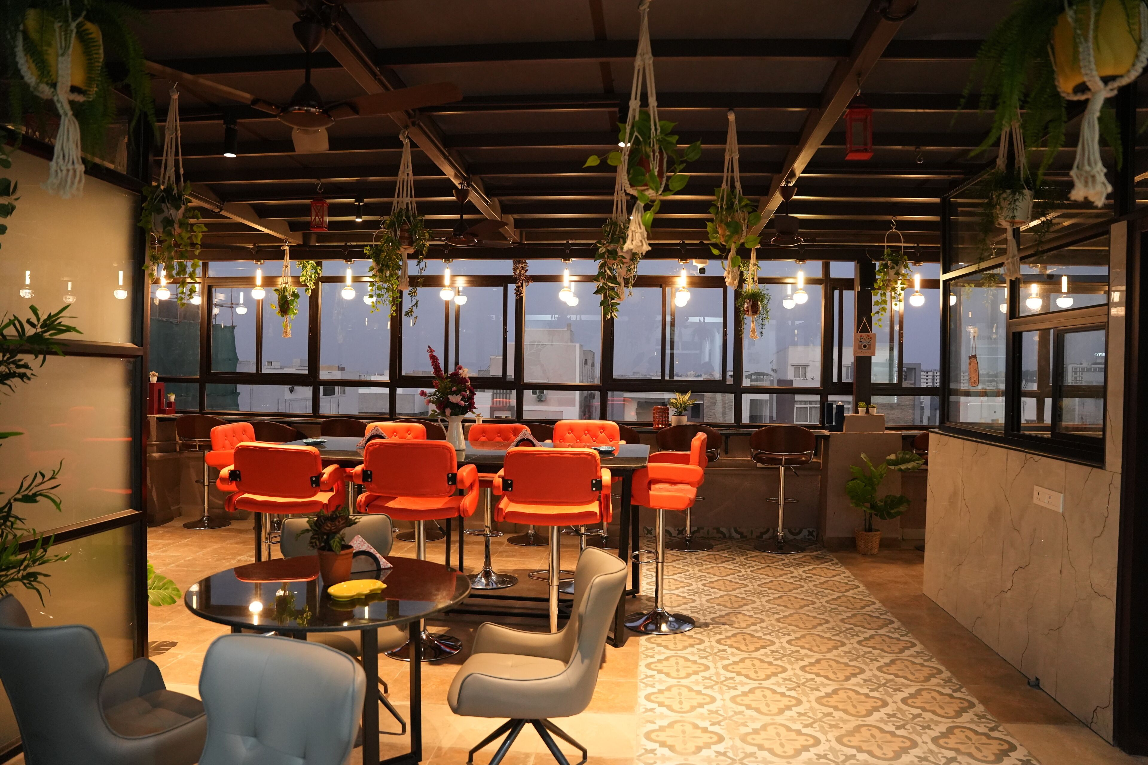 A modern interior with a high ceiling, hanging plants, and a city view through large windows.