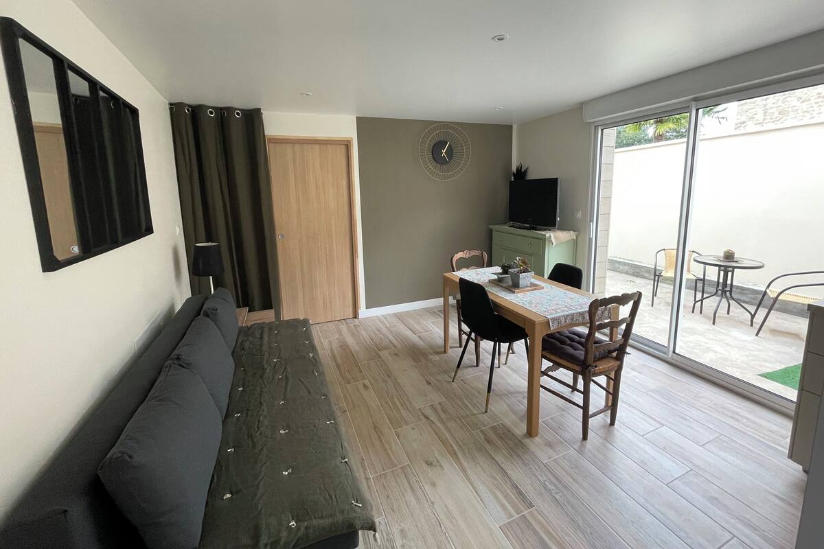 A compact living space with a sofa, a dining table with chairs, a TV, and a sliding glass door leading to an outdoor area with a table and chairs.