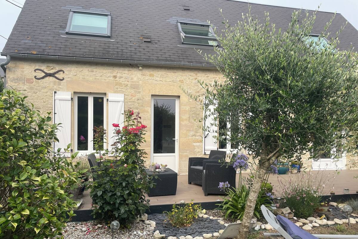 A house with a stone facade, a tiled roof, and a garden with a patio area.