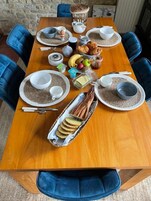 Una mesa de madera dispuesta con platos, tazones, cubiertos, pan, frutas y aderezos.