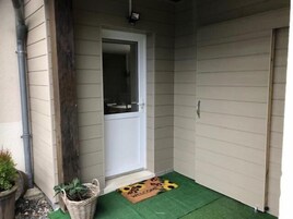Un pequeño porche con una puerta, un felpudo y una planta en maceta.