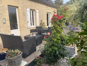 A stone building with a patio area featuring wicker furniture and potted plants. - LE DOUX REFUGE (Esquay-sur-Seulles)