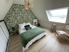 Un dormitorio con una cama, una ventana, una silla y una mesita.