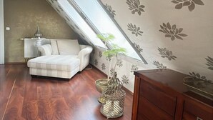 Una habitación con techo inclinado, un sofá blanco, un armario de madera y una planta decorativa en una maceta de metal.