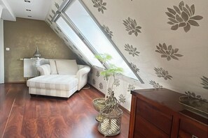 Una habitación con techo inclinado, un sofá blanco, un armario de madera y una planta decorativa en una maceta de metal.